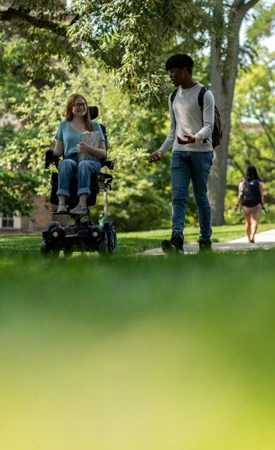 A student in a wheelchair smiling and talking with another student on MSU's campus